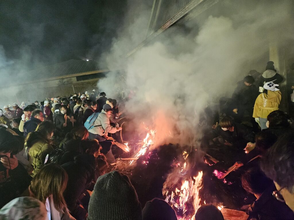 2026年太宰府天満宮鬼すべ神事の後、煤のついた木片を観覧者たちが拾っている様子。大量の煙と炎の迫力で、神事を疑似体験できる。