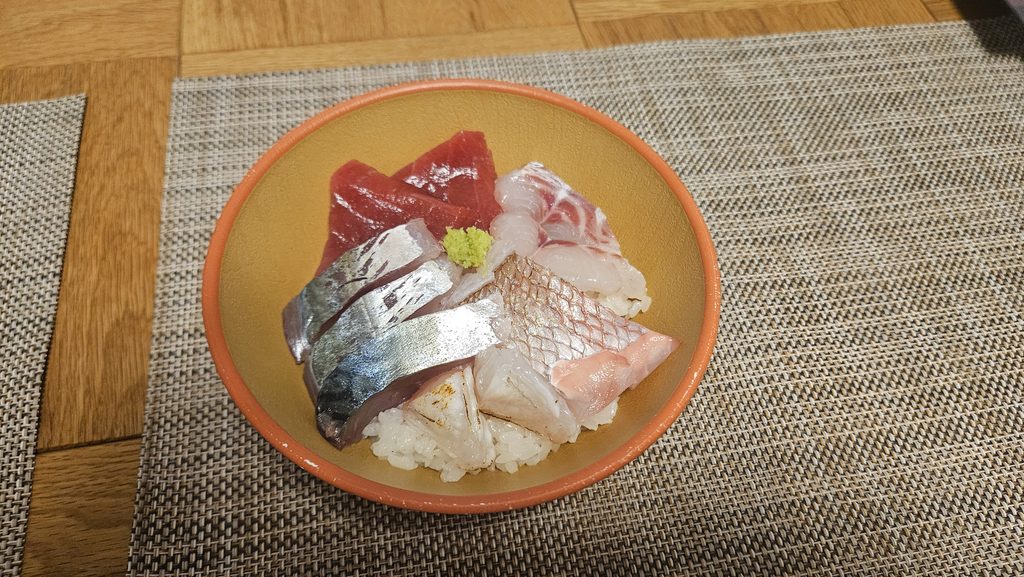 太宰府天満宮近く鮮魚いの吉のお刺身をテイクアウトしたものを自宅で海鮮丼にした写真。
どんぶりの中に酢飯とマグロ、鯛、アジ、ふぐの湯引き、白身の炙りがのっている。